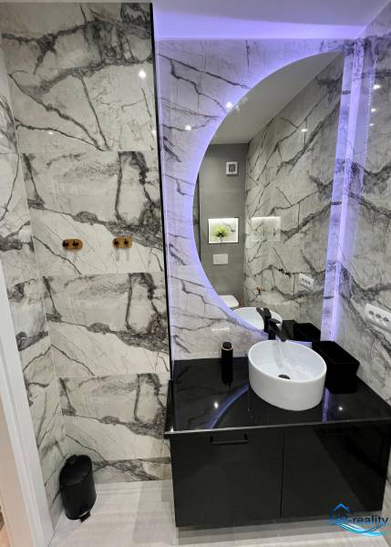 Koupelna v Rekreačním apartmánu s kulatým zrcadlem a elegantními obklady.