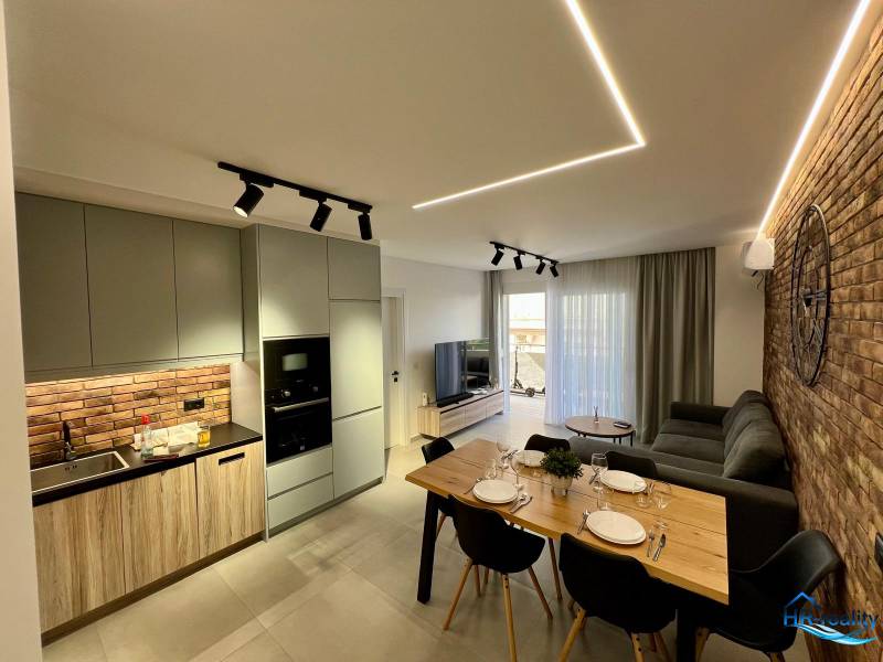 Obývací pokoj s kuchyní v rekreačním apartmánu. Cihlová stěna, jídelní stůl a pohodlná sedačka.