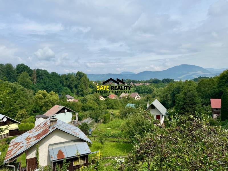 Venkovská chalupa v Mojši obklopená zelení a kopci pod modrou oblohou.