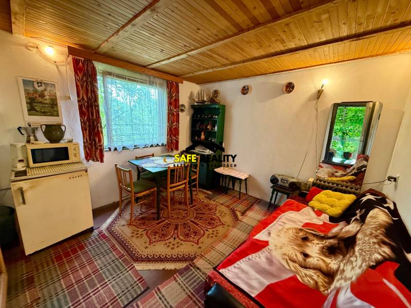 V chatě s dřevěným stropem se nachází stůl, židle a starožitná lednička.