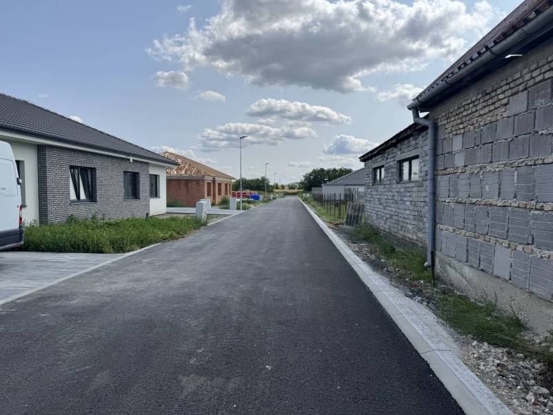 Rodinné domy se stavbou a asfaltovou cestou v Horním Baru pod oblačnou oblohou.