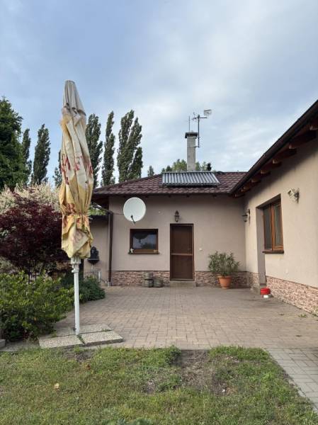 Rodinný dům v Malackách, přední dvůr s terasou, zelení a satelitní anténou.