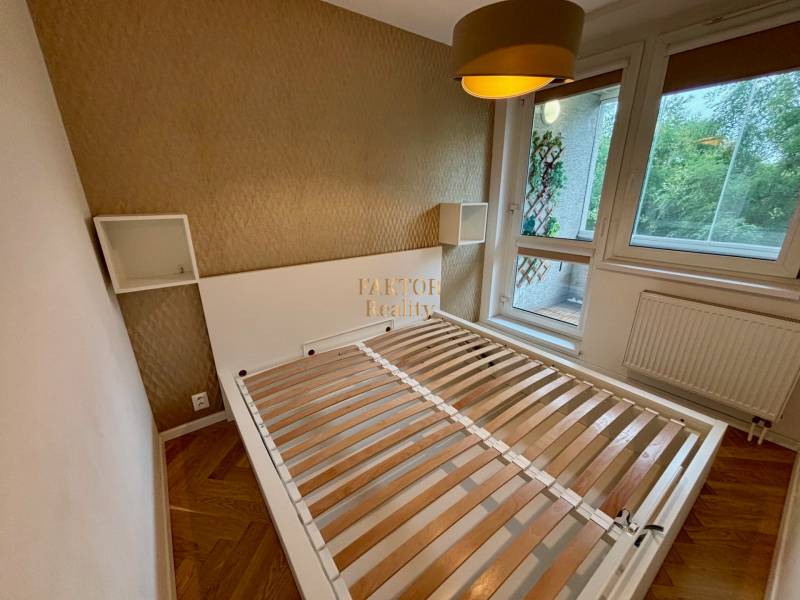 Ložnice v dvoupokojovém bytě s postelí, tapetou, oknem a francouzským balkonem.