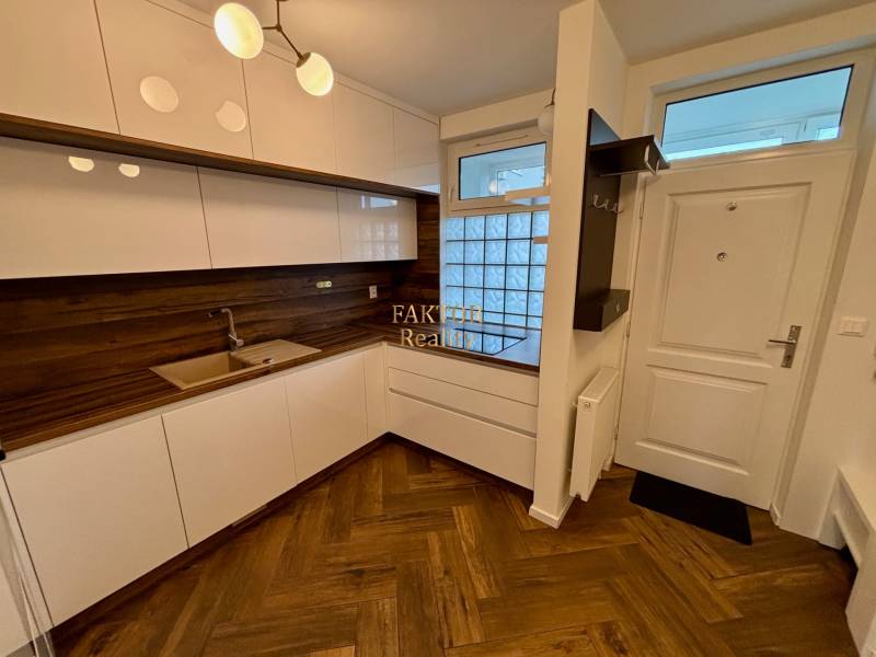 Kuchyně v 2-pokojovém bytě s dřevěnými podlahami a moderními bílými skříňkami.