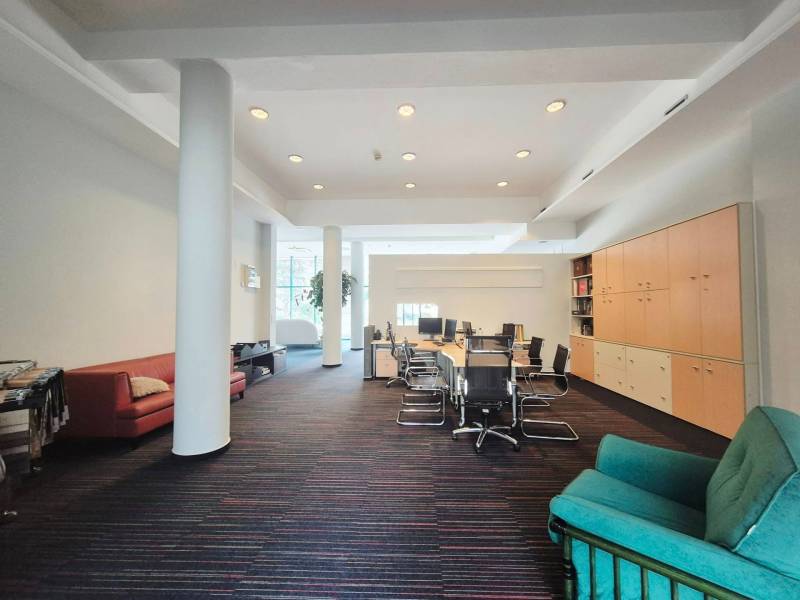 Kancelářský prostor s velkým stolem, židlemi, sedačkami, skříňkami a kobercovou podlahou.