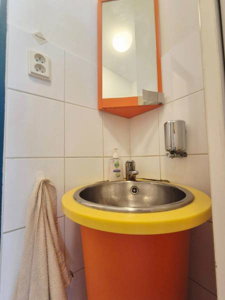 Oranžové umyvadlo s kulatým žlutým okrajem, zrcadlo a věšák s ručníkem.