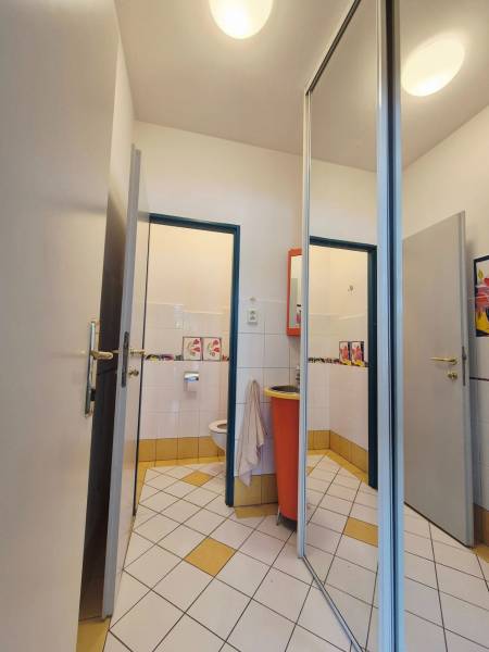 Toaleta s bílými a žlutými dlaždicemi a oranžovým umyvadlem v obchodních prostorách.