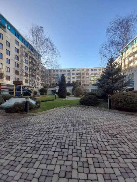 V Bratislavě - Novém Městě na Vajnorské uličce s obchodními prostory jsou stromy a udržovaná dlažba.