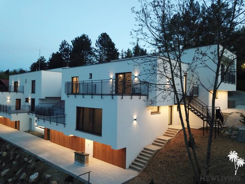 Na obrázku je osvětlená budova se stromy, schody a vícebytovou architekturou.