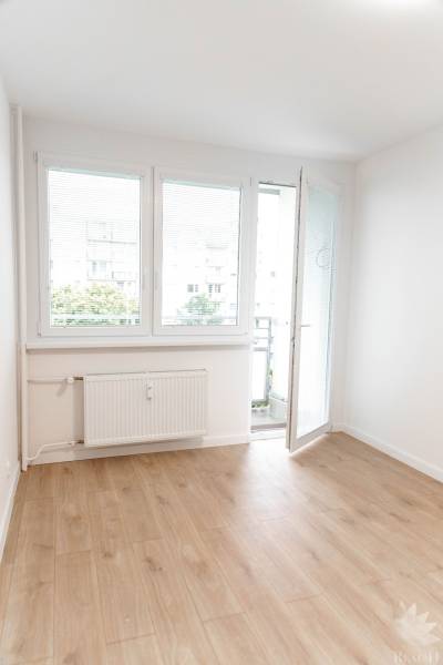 Ve 2-pokojovém bytě je světlá místnost s balkónovými dveřmi a dřevěnou podlahou.