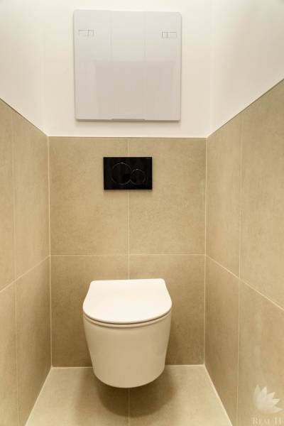 Závěsné WC v 2-pokojovém bytě, béžové obklady, černé splachovací tlačítko.