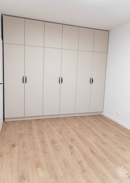 Bílá vestavěná skříň se šesti dveřmi v 2-pokojovém bytě na dřevěné podlaze.