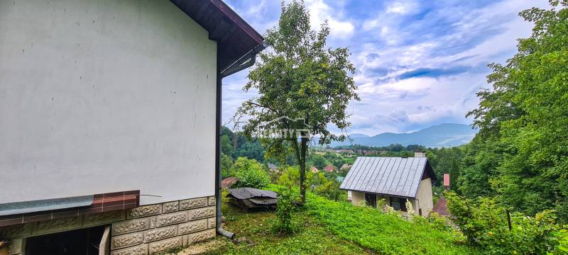 Výhled z chaty v Mojši ukazuje střechy, zeleň a vzdálené kopce pod oblačnou oblohou.