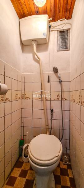 Malá koupelna v chatě s toaletou, obklady a dřevěným stropem.