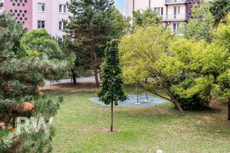 Park v Bratislavě na Československých parašutistů s lavičkou a zelení, obklopený bytovými domy.