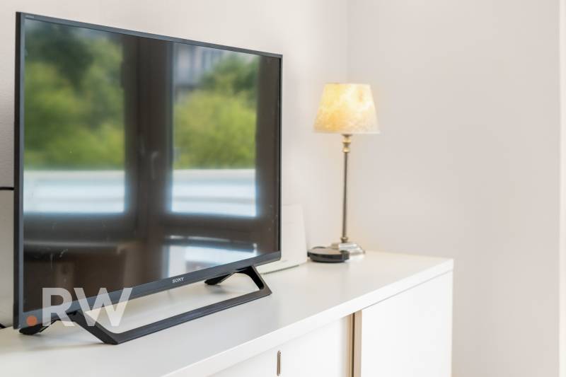 Televizor a lampa na bílé komodě v 2pokojovém bytě.