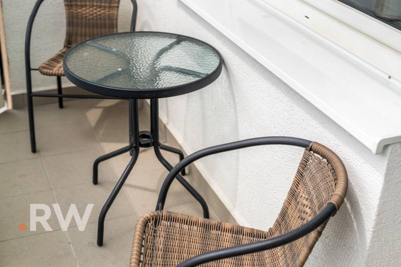 Balkon s ratanovými židlemi a skleněným stolem v 2-pokojovém bytě.