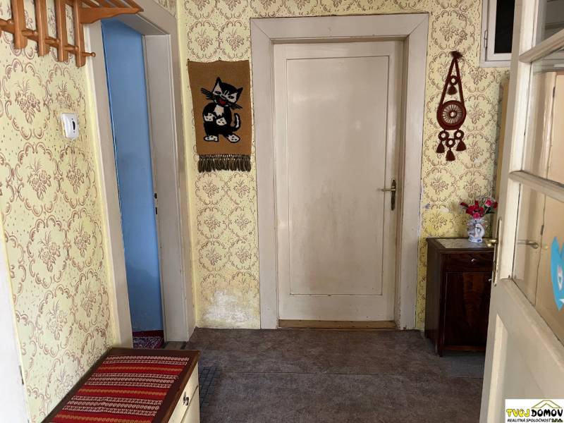 Chodba v rodinném domě s tapetami, dřevěným nábytkem a dekoracemi na stěnách.