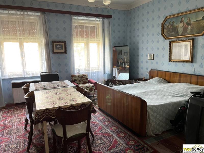 Interiér rodinného domu s ložnicí, stolem, starožitným nábytkem a dekoracemi na stěnách.