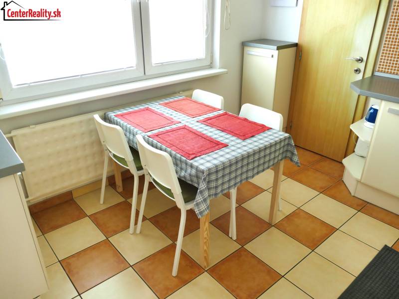Jídelna s dřevěným stolem a čtyřmi židlemi ve 3-pokojovém bytě, kostkovaná podlaha.