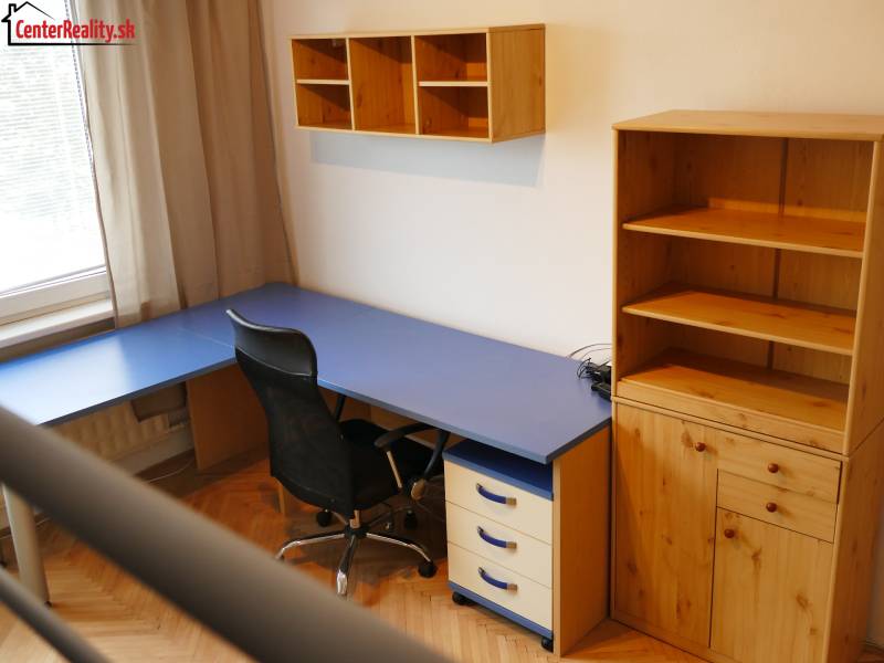 Domácí kancelář s modrým stolem a dřevěným úložným nábytkem v 3-pokojovém bytě.
