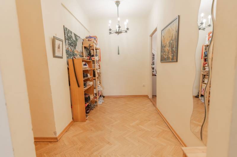 Chodba ve 4pokojovém bytě s policemi na boty a podlahou s dřevěným dekorem.