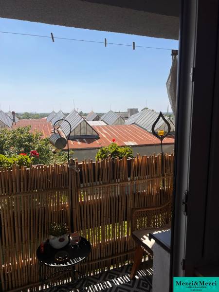 Balkon v 3-pokojovém bytě s ratanovým nábytkem a výhledem na střechy.