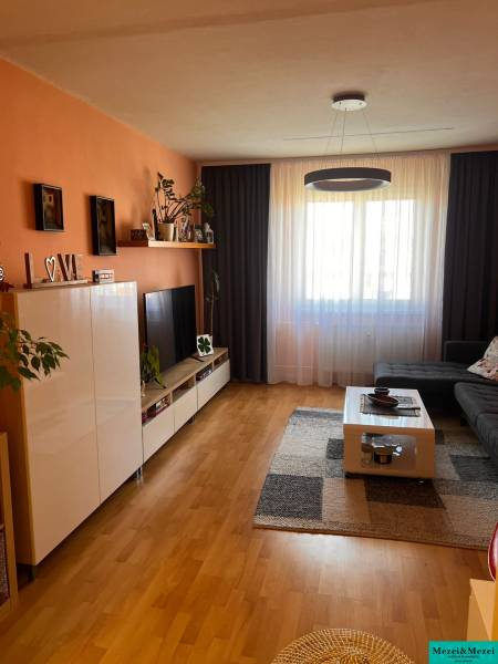 Obývací pokoj s oranžovou stěnou, tmavými závěsy, velkým oknem a nábytkem v třípokojovém bytě.