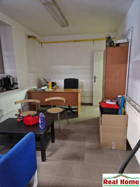 Kancelář na Šamorínské s nábytkem, obsahuje stůl, police a kancelářské potřeby.