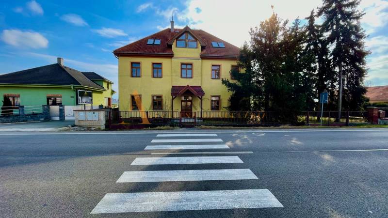 Budova na ulici Chrabrany v Topoľčanech, naproti přechodu pro chodce a stromům.