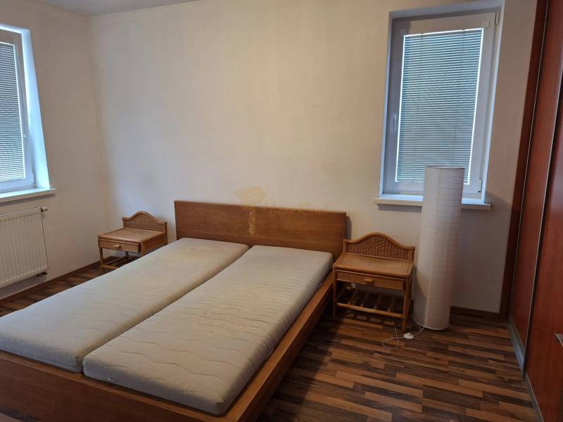 Ložnice v dvoupokojovém bytě s dřevěnou postelí a nočními stolky.