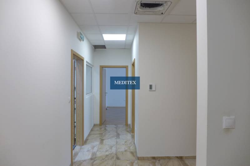 Bílá chodba s dlažbou, dřevěnými dveřmi a osvětlením v areálu skladů a hal.