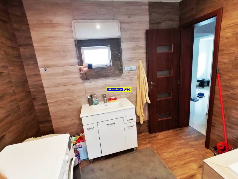 Koupelna v rodinném domě se zrcadlem, skříňkou, umyvadlem a pračkou.