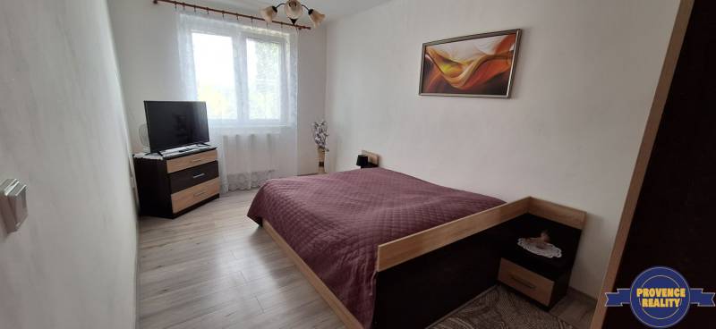 Ložnice v 3-pokojovém bytě s postelí, televizí a dekorací na stěně.