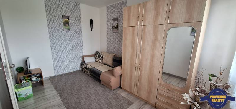 Obývací pokoj v 3pokojovém bytě s pohovkou, skříní a dekoracemi na stěně.