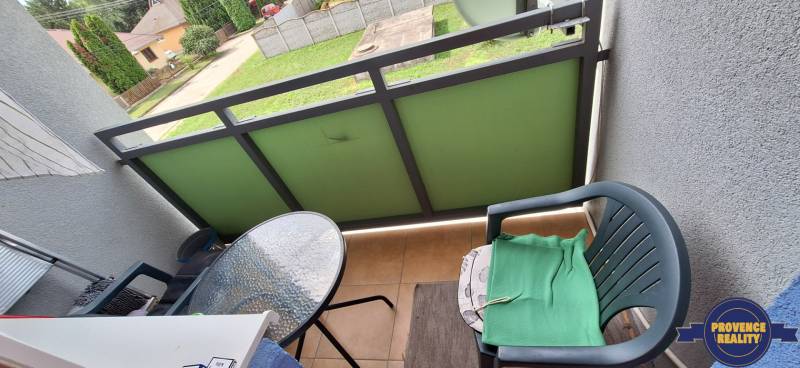 Balkon 3-pokojového bytu s plastovou židlí a malým skleněným stolkem.