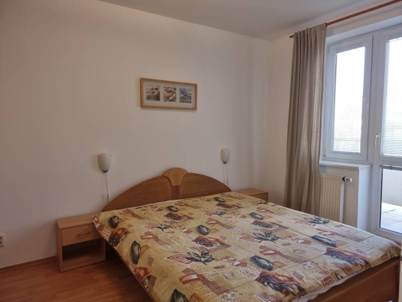 Ložnice ve 4pokojovém bytě s manželskou postelí, obrazem a balkónovými dveřmi.