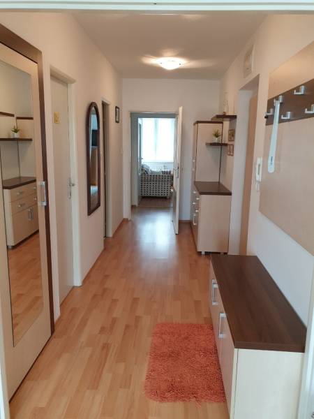 Chodba 4pokojového bytu s dřevěnou podlahou, zrcadlem a skříňkami na stěně.