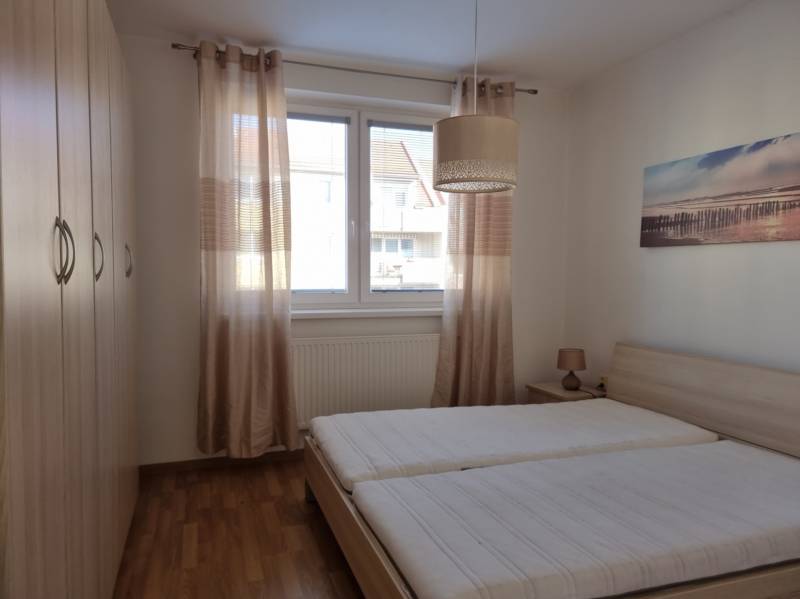 Ložnice s dvěma postelemi, vestavěnou skříní a obrazem v dvoupokojovém bytě.