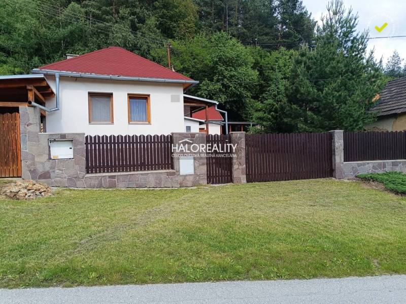 Chata v Helcmanovcích s dřevěným plotem a upraveným trávníkem obklopená zelení.