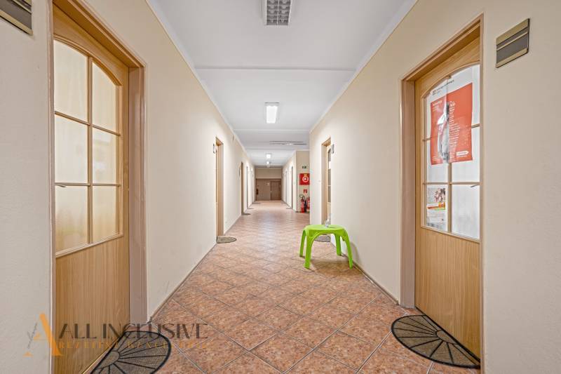 Chodba s dveřmi, dlažbou a zelenou židlí v kancelářích.