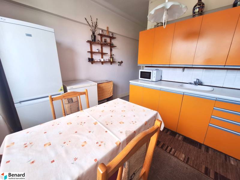 Kuchyně v 2-pokojovém bytě s oranžovou linkou, bílou lednicí a jídelním stolem.