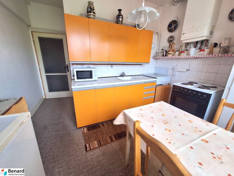 Kuchyně s oranžovou linkou a jídelním stolem v 2-pokojovém bytě.