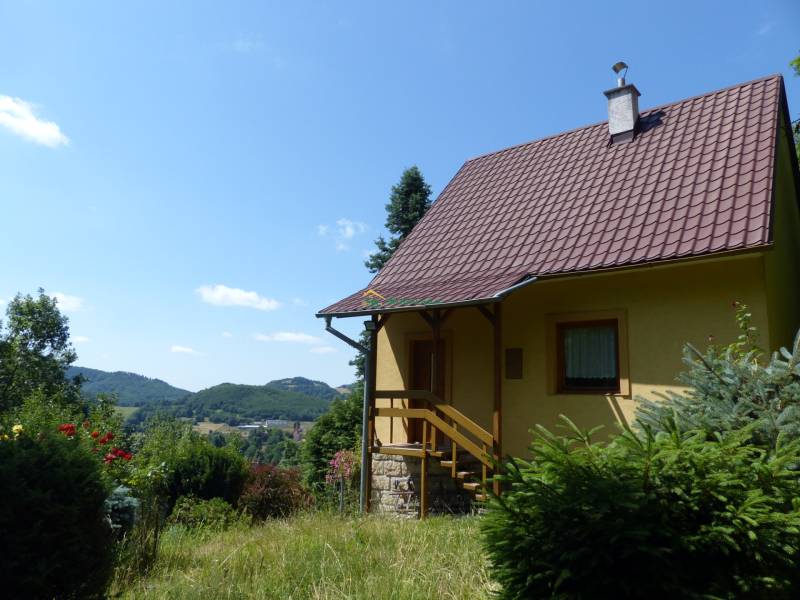 Chata v Štiavnických Baniach, obklopená zelení a s výhledem na kopce v pozadí.