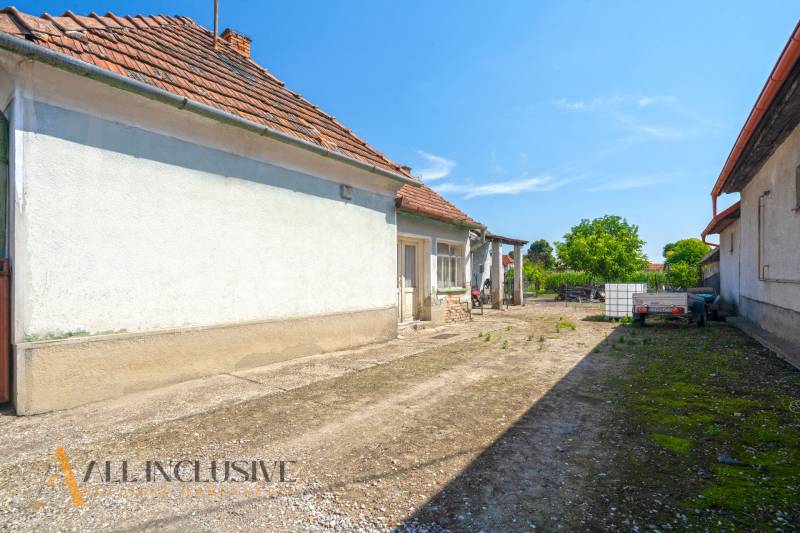 Dvor rodinného domu v Jahodné s přívěsem, nádrží a zelení.