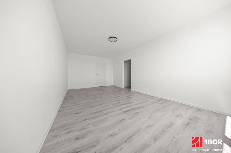 Prostorný pokoj s laminátovou podlahou a bílými stěnami ve 2pokojovém bytě.