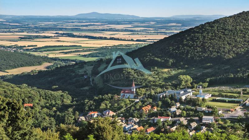 Panoramatický pohled na vesnici v údolí, obklopenou lesy a poli. Pozemky vhodné k bydlení.