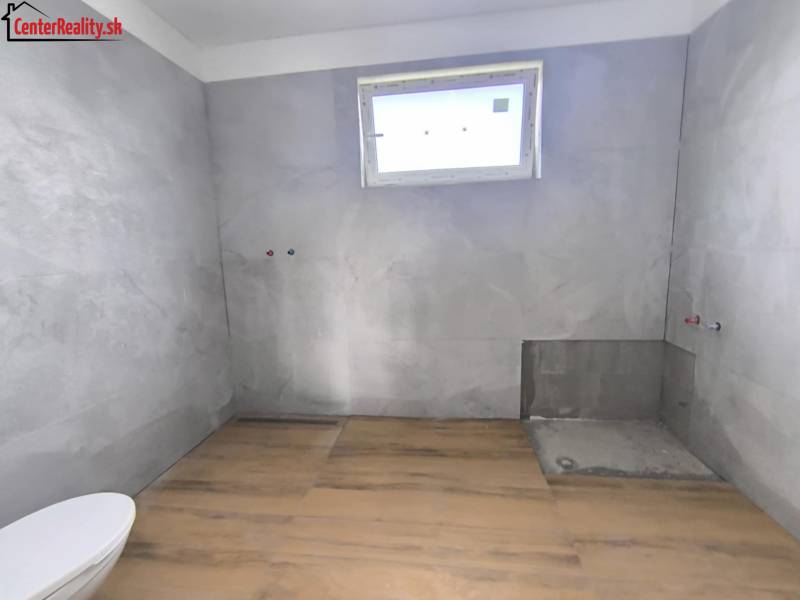 Koupelna v rodinném domě s dlažbou, připravená k instalaci, světlo přes malé okno.
