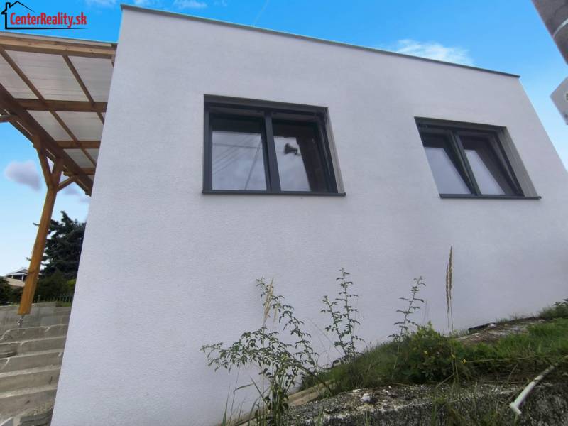 Rodinný dům v Malých Kršteňanech s dvojicí velkých oken a dřevěným přístřeškem.