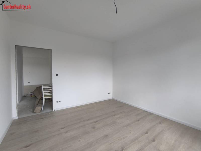 Prázdný pokoj s bílými stěnami a světlou dřevěnou podlahou v rodinném domě.